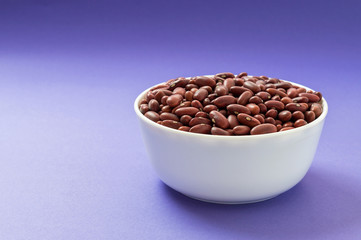 Raw red kidney bean in a bowl on violet background