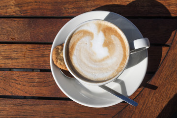 Coffee cup with cappuccino and milk foam on a wooden table outdoors in summer, view from above, copy space