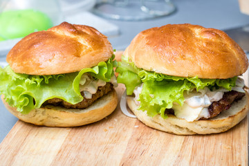 Close-up photo of home made hamburger with beef, onion, tomato, lettuce, cheese and spices. Fresh burger closeup on wooden rustic table with potato fries and chips.