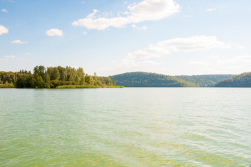 Forest on the bank of the lake . White clouds reflect in the water