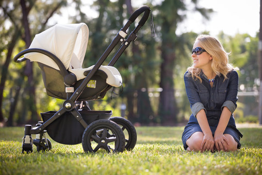 Young woman with her newborn baby enjoying sunny summer day in the park. Mother with child in the stroller outdoors. Motherhood.  Mum with baby walking in the city.