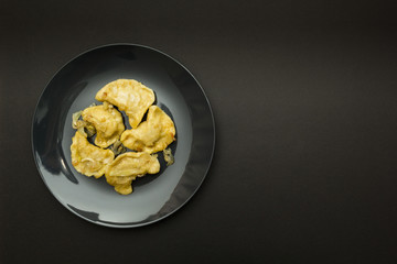 Black plate with pierogies on a black background. Place for the text.