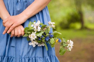 Close-up of woman's hand holding a branch of blooming apple tree. Blues dress as a background.Spring concept.