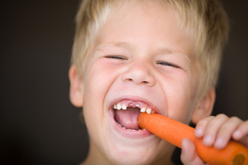 Portrait of cute toothless kid boy eating carrot. Happy child with vegetable. Healthy eating.