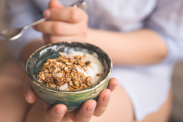 Young woman with muesli bowl. Girl eating breakfast cereals with nuts, pumpkin seeds, oats and yogurt in bowl. Girl holding homemade granola. Healthy snack or breakfast in the morning.