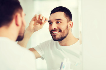 man with tweezers tweezing eyebrow at bathroom