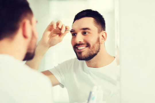 Man With Tweezers Tweezing Eyebrow At Bathroom