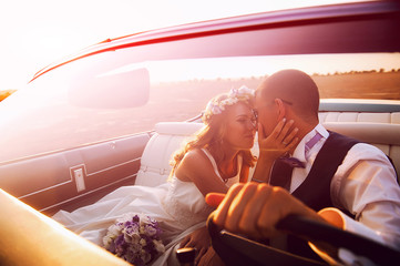 Young loving couple in a cabriolet at sunset