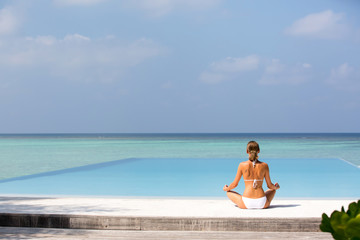 Meditation. Photo of a woman who is sitting in the lotus position on the ocean coast. Maldives