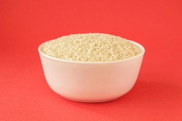 Raw medium grain rice in a bowl on red background