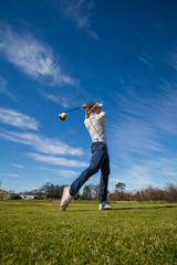 Wide angle view of a golfer teeing off from a golf tee on a bright sunny day on a golf course in...