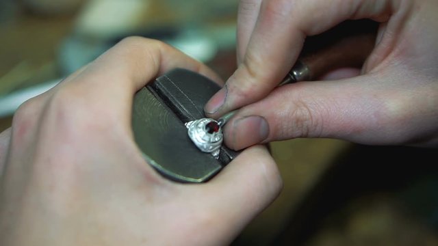Red gem fixing in the center of a silver ring using tool