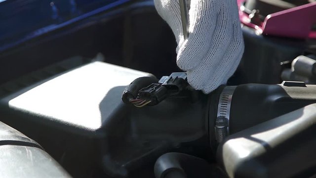 The man disconnect a connector and takes out the oxygen sensor under the open hood
