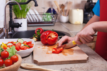 Child hands chopping a red bellpepper for a fresh vegetables salad