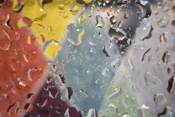 Drops on glass, colored abstract blurred light background. Rain drops on glass, view from the window.