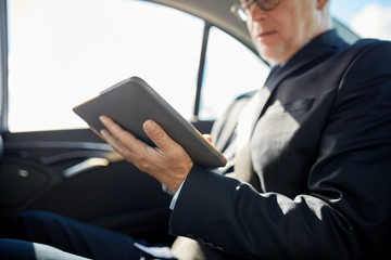 senior businessman with tablet pc driving in car