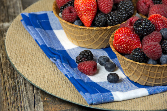ripe berries in waffle bowl on blue and white checkered napkin and burlap plate
