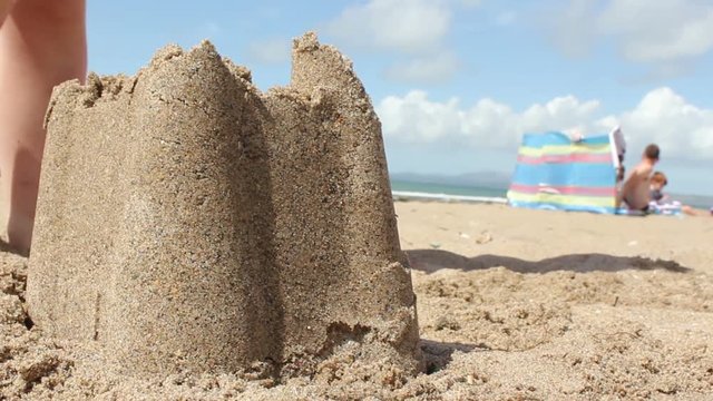 Young boy making a sandcastle on pretty beach and then stamps on it