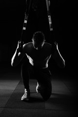 One young handsome brave curly bearded muscled man with a beard makes Total Resistance eXercises fitness trx straps working out in gym crossfit black and white stylised.