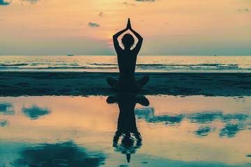 Yoga Silhouette. Woman on the beach with reflection in water.