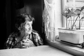 Naklejka na ściany i meble An elderly woman pining at the window. Black-and-white photo.