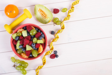 Fresh fruit salad and centimeter with dumbbells, healthy lifestyle and nutrition concept