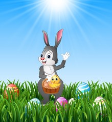 Easter bunny holding a basket with easter egg and chick in the grass background 