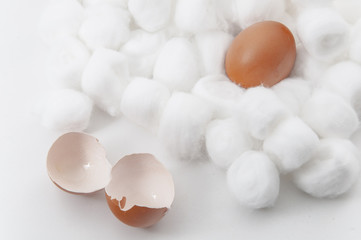 Concept image of broken chicken eggshell outside of place with soft and safety cotton balls surface