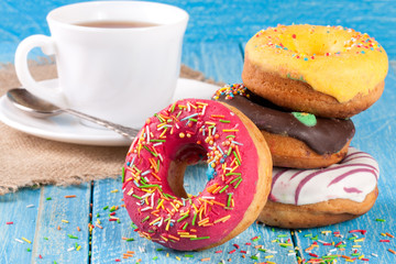 pile of glazed donuts with a cup of tea on a blue wooden background