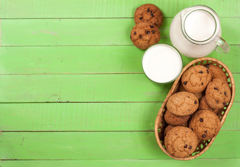 jug and glass of milk with oatmeal cookies on a green wooden background with copy space for your text. Top view