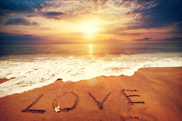 Inscription LOVE written on the sandy beach with ocean wave - sunset time. Honeymoon concept. vintage color tone effect