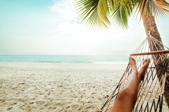 Leisure in summer - Beautiful Tanned legs of sexy women. relax on hammock at sandy tropical beach. vintage color styles