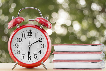 alarm clock and notebook with abstract nature blur background, defocused green leaves.