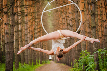 Beautiful and graceful aerial gymnast performs exercises on the air ring in the woods