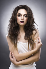 beauty portrait of the young woman in a white undershirt with a vanguard make-up and a flowing hair on a gray background