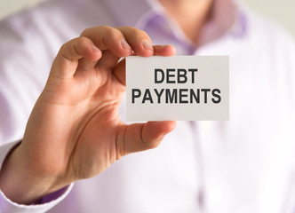 Businessman holding a card with DEBT PAYMENTS message