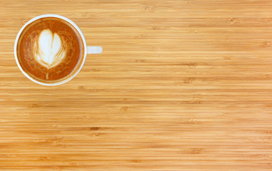 Top view of a coffee with heart pattern in a white cup on bamboo wooden background