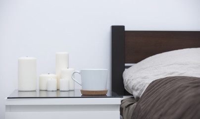 cup of coffee and white set of candles on the table near bed in the cozy bedroom