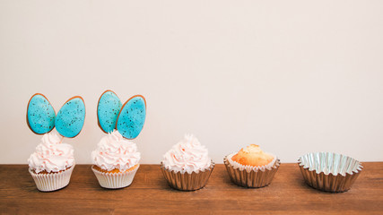 Delicious cupcakes with white cream and blue cakepops in row placed on wooden surface. White background with copyspace for text. Concept of creating sweets. Baking and cake decorating timeline