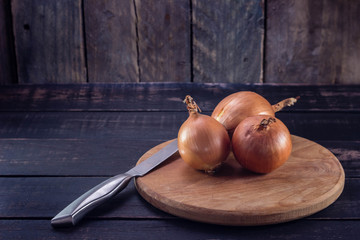 Onions on a cutting board with knife on dark wooden background