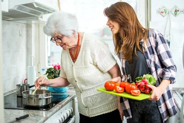 Crédence de cuisine en verre imprimé Cuisinier Grand-mère et sa petite-fille cuisinent ensemble dans la cuisine.