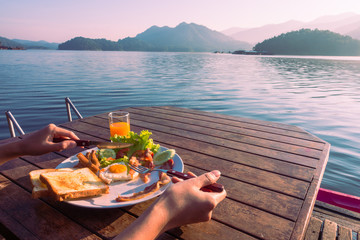 Close up cute girl eating breakfast food with orange juice on wooden table at beautiful lake ,Mae...