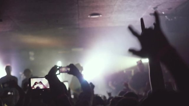 Fans waving their hands and hold the phone with digital displays recording video at rock concert in a night club in slow motion. 1920x1080