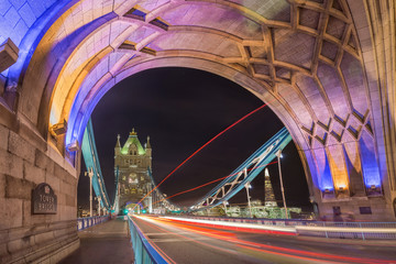 Obraz premium London, England - Night shot of the world famous colorful Tower Bridge in London with double decker bus light trails and offices and Shard skyscraper at background