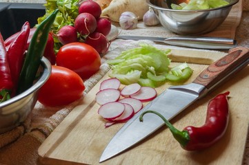 Cooking with fresh vegetables sliced with a knife on a wooden Board radish celery   salad, red pepper cabbage tomato chili onion garlic