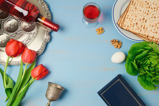 Passover holiday concept seder plate, matzoh, tulip flowers and wine bottle on wooden background. Top view from above