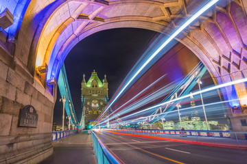 Obraz premium London, England - Night shot of the world famous colorful Tower Bridge in London with double decker bus light trails and offices and Shard skyscraper at background