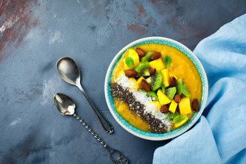 Mango smoothie bowl with pieces of kiwi, mango, coconut shavings and chia seeds on a stone background. Selective focus.