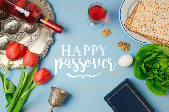 Jewish holiday Passover Pesah greeting card with seder plate, matzoh, tulip flowers and wine bottle on wooden background. View from above