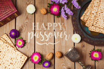Jewish holiday Passover greeting card with matza and seder plate over wooden background. View from above